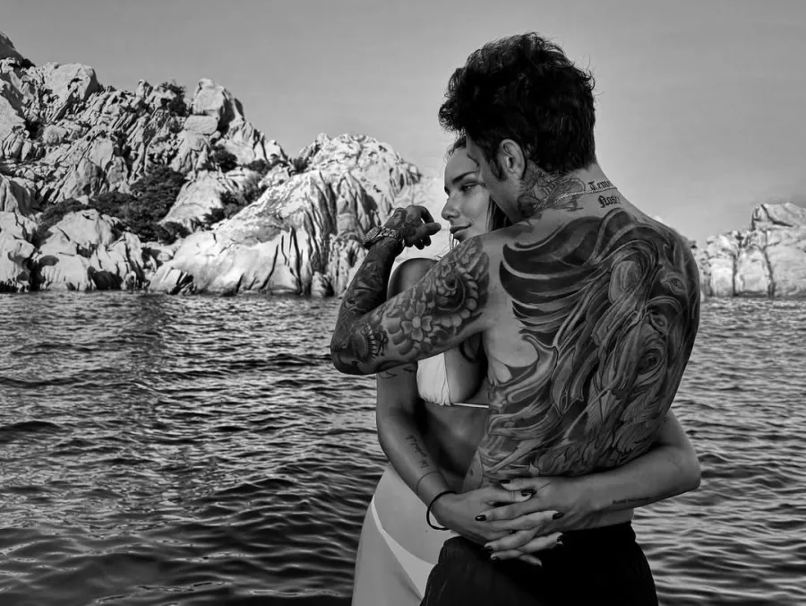 Ο Fedez και η Giulia Honegger αγκαλιάζονται τρυφερά σε ένα σκάφος με φόντο βραχώδη τοπία, δείχνοντας τη νέα τους σχέση.