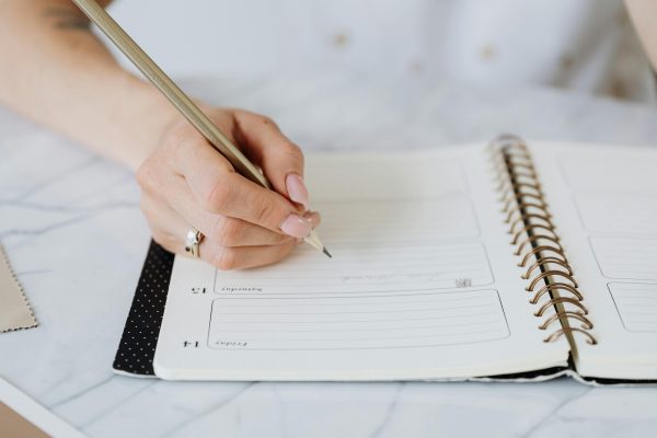 Γυναικείο χέρι με μολύβι γράφει σε ένα bullet journal, βοηθώντας στην οργάνωση της καθημερινότητας.