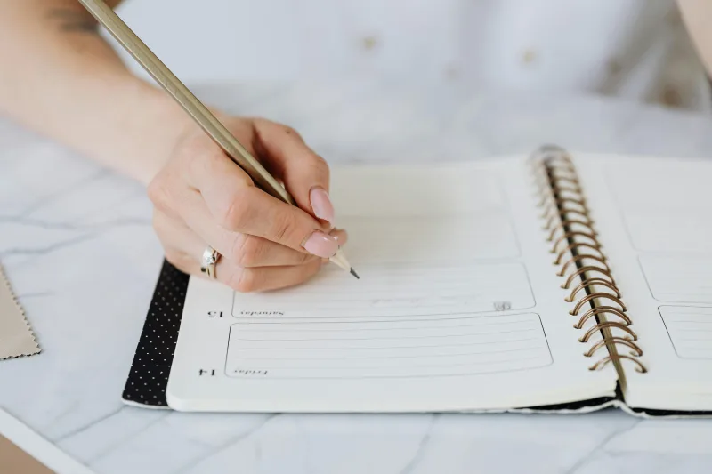 Γυναικείο χέρι με μολύβι γράφει σε ένα bullet journal, βοηθώντας στην οργάνωση της καθημερινότητας.