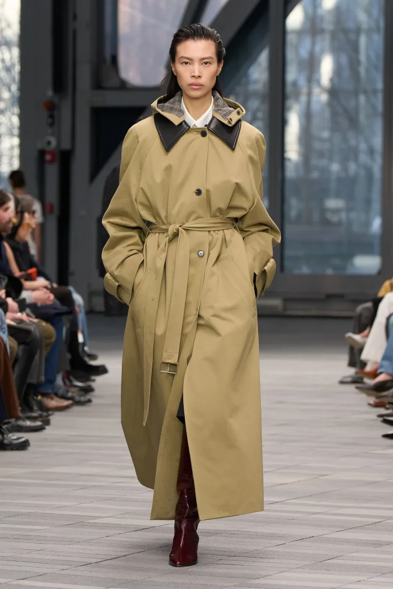 Μοντέλο παρουσιάζει το νέο trench coat trend με ζώνη στη μέση και δερμάτινο γιακά, σε πασαρέλα οίκου μόδας.