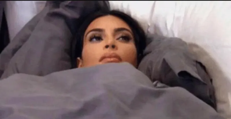 Η Kim Kardashian ξαπλωμένη στο κρεβάτι κάτω από τα σκεπάσματα με βλέμμα απόγνωσης.
