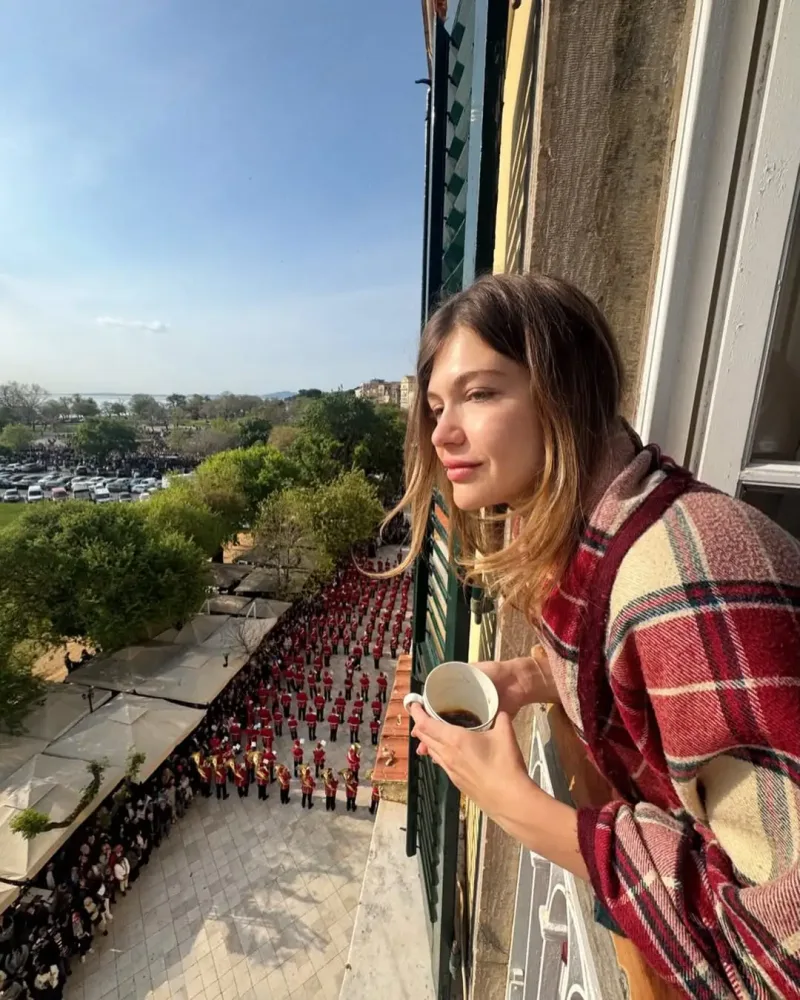 Γυναίκα με καρό ριχτάρι απολαμβάνει τον καφέ της παρακολουθώντας την παρέλαση των Ελλήνων celebrities το Πάσχα 2026.