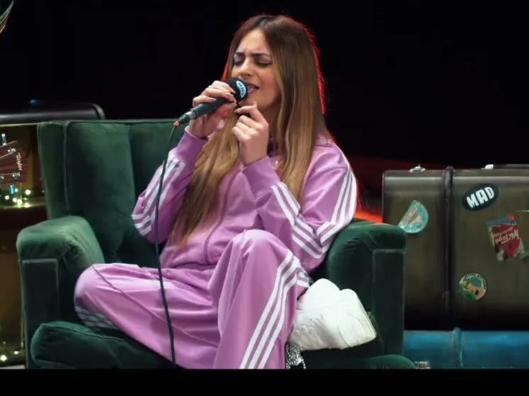 Η Daphne Lawrence τραγουδάει στο Unplugged Stories φορώντας μωβ φόρμα, με έναν κιθαρίστα δίπλα της.