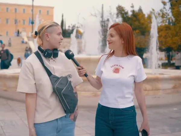 Δύο γυναίκες συνομιλούν με μικρόφωνο του MAD έξω από ένα κτίριο με κολώνες και συντριβάνι, σε συνέντευξη για το «κοινωνικό φίλτρο».