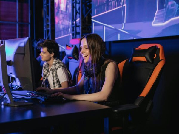Δύο νεαρά άτομα παίζουν βιντεοπαιχνίδια σε gaming καρέκλες.