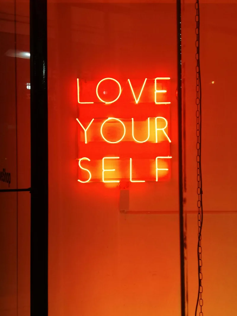 Φωτεινή επιγραφή νέον με το μήνυμα "LOVE YOUR SELF" σε πορτοκαλί φόντο, σχετική με την αυτοεκτίμηση και τη βελτίωση της ζωής.