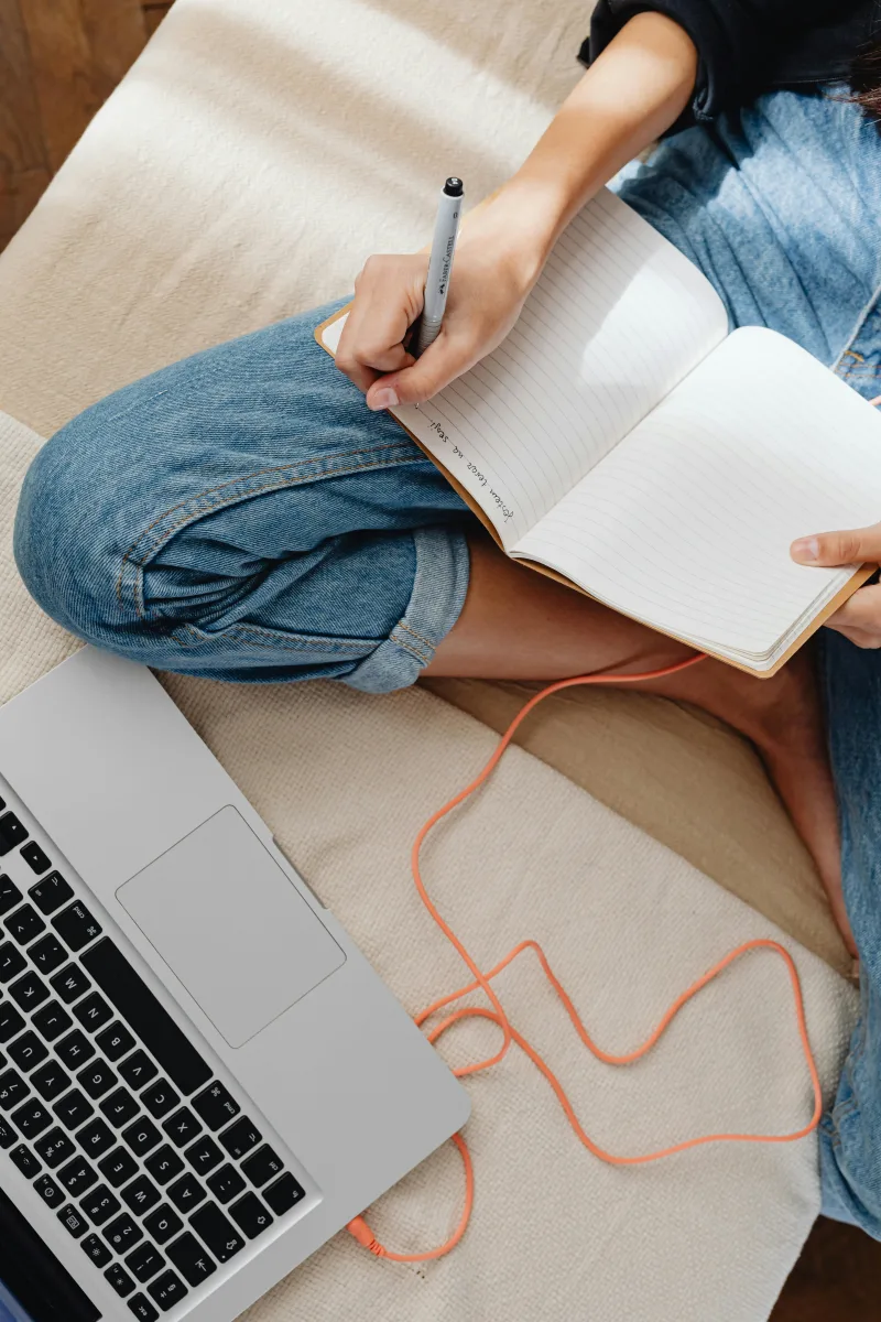 Γυναίκα γράφει σε σημειωματάριο δίπλα σε laptop, εστιάζοντας σε πράγματα που βελτιώνουν τη ζωή της.