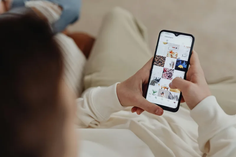 Χέρια που κρατούν smartphone και περιηγούνται σε προφίλ social media, σχετικό με τα ζώδια που παρακολουθούν online.