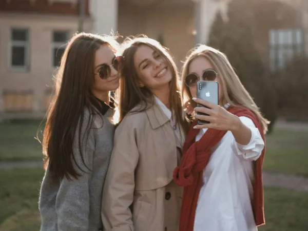 Τρεις νεαρές γυναίκες βγάζουν selfie με smartphone σε εξωτερικό χώρο.