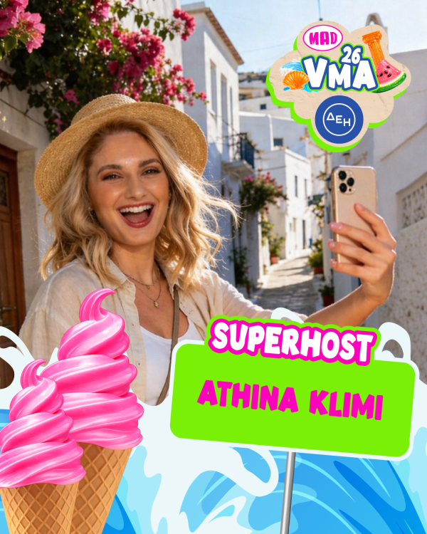 Η Αθηνά Κλίμη ως superhost των MAD VMA 2026 ποζάρει με το κινητό της σε ένα γραφικό ελληνικό σοκάκι.