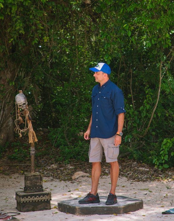 Ο Σηφάκης του Survivor στέκεται δίπλα σε ένα τελετουργικό αντικείμενο, φορώντας καπέλο και κοντομάνικη μπλούζα.