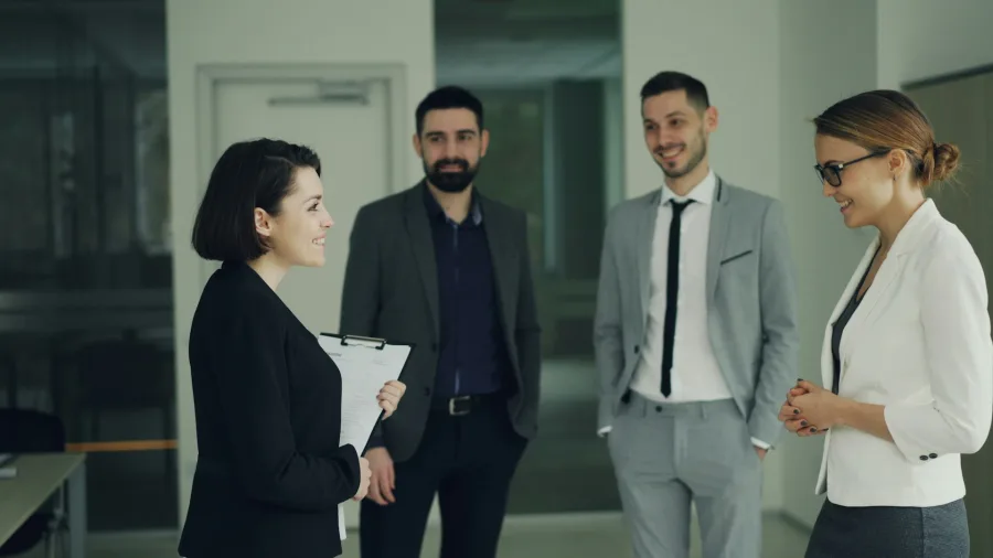 Τέσσερις επαγγελματίες συζητούν σε έναν διάδρομο, εστιάζοντας στην ισορροπία και την επικοινωνία στον χώρο εργασίας.