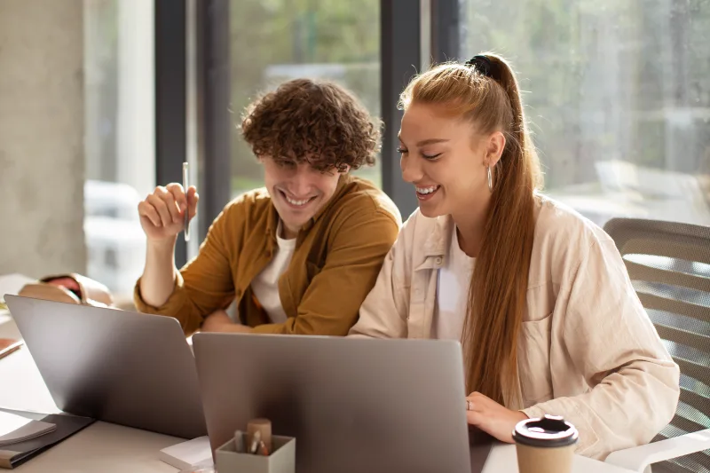 Νεαρή γυναίκα και άνδρας συνεργάζονται σε laptops, δείχνοντας τις διαφορές Gen Z και Millennials στην εργασιακή κουλτούρα.