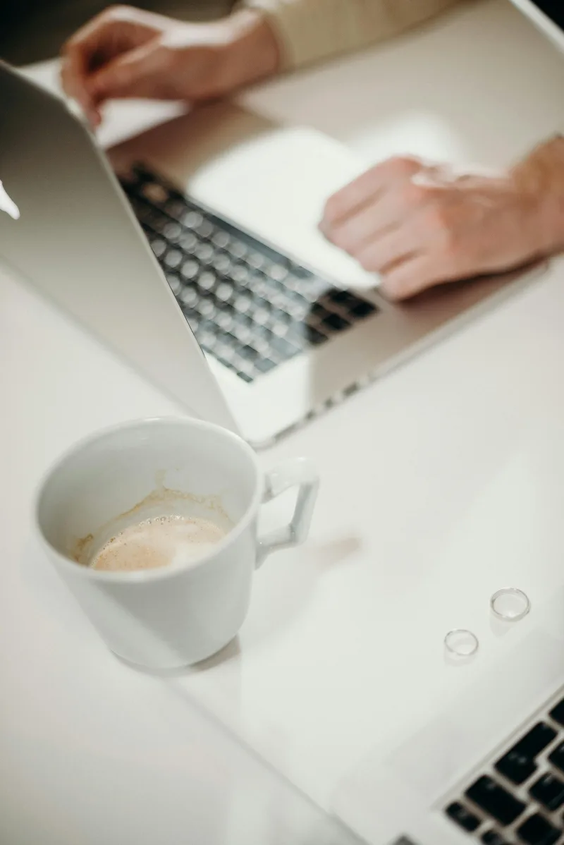Άνθρωπος που εργάζεται σε laptop με φλιτζάνι καφέ δίπλα, αναδεικνύοντας τις διαφορές Gen Z και Millennials στην εργασιακή κουλτούρα.