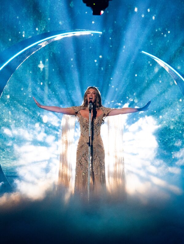 Η Delta Goodrem τραγουδάει στη σκηνή της Eurovision 2026 με εντυπωσιακό φόρεμα και φόντο με ουράνιο τόξο.