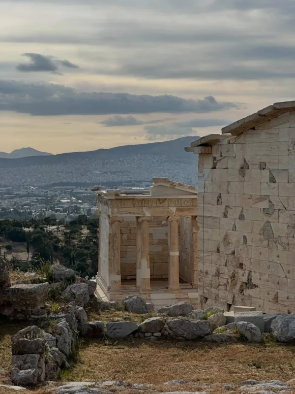 Αρχαίο μνημείο με κολόνες και θέα στην Αθήνα, θυμίζοντας καλοκαίρι στο Αιγαίο.