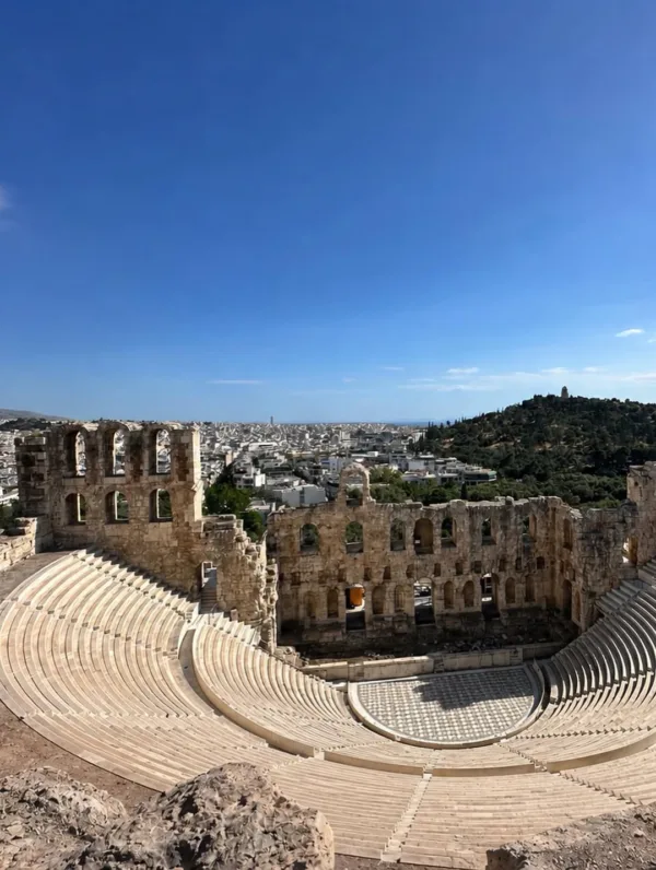 Το Ωδείο Ηρώδου του Αττικού στην Αθήνα, με φόντο την πόλη, σε μια ηλιόλουστη μέρα.