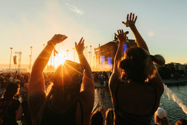 Χαρούμενοι θεατές απολαμβάνουν το Mad Summer Festival με τα χέρια υψωμένα στον αέρα κατά τη δύση του ηλίου.