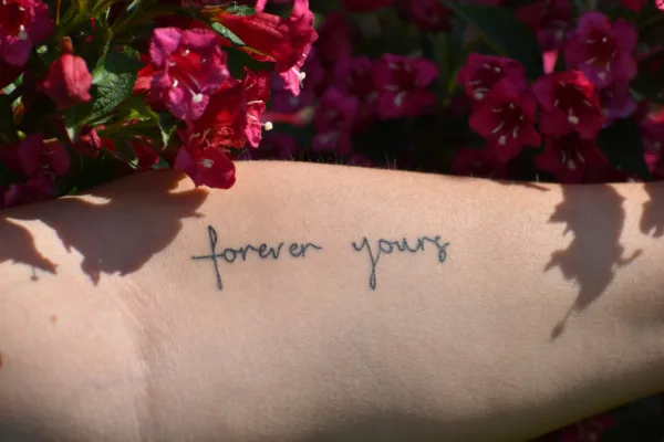 Το πρώτο σου tattoo με τη φράση "forever yours" σε συνδυασμό με ροζ λουλούδια και σκιές φύλλων.