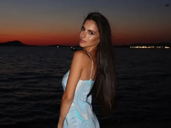 Η Αλεξάνδρα Νίκα ποζάρει με το φόρεμά της δίπλα στη θάλασσα κατά τη δύση του ηλίου.
