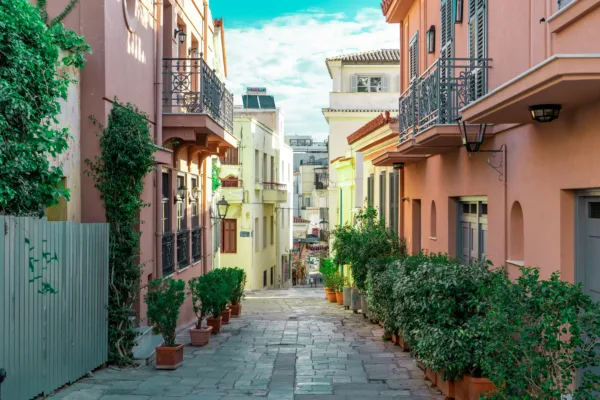 Πολύχρωμα σπίτια και φυτά σε πετρόχτιστο δρόμο της Αθήνας, ιδανικό για δροσιά το καλοκαίρι.