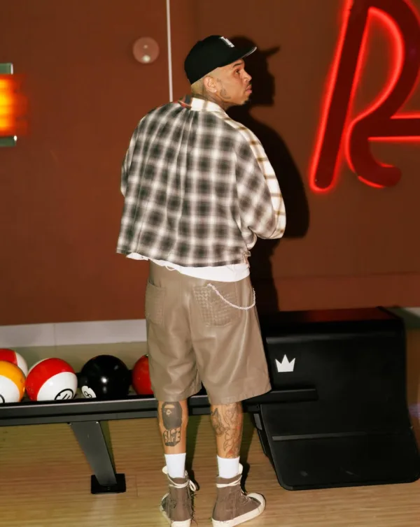 Ο Chris Brown ποζάρει με καπέλο και καρό πουκάμισο δίπλα σε μπόουλινγκ μπάλες, προετοιμάζοντας την επιστροφή του με νέα τραγούδια.