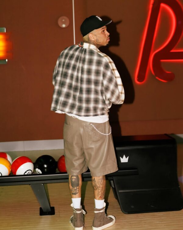 Ο Chris Brown ποζάρει με καπέλο και καρό πουκάμισο δίπλα σε μπόουλινγκ μπάλες, προετοιμάζοντας την επιστροφή του με νέα τραγούδια.