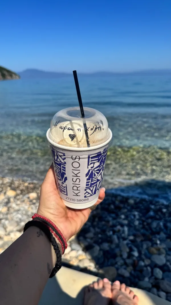 Δανάη Μπάρκα κρατάει καφέ στην παραλία με φόντο τη θάλασσα, ενώ ετοιμάζεται για τον γάμο της.