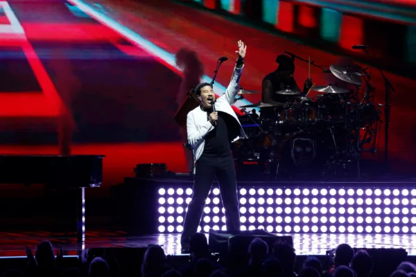 Ο Lionel Richie τραγουδάει στη σκηνή με ενθουσιασμό, ενώ πίσω του διακρίνεται ο drummer του.