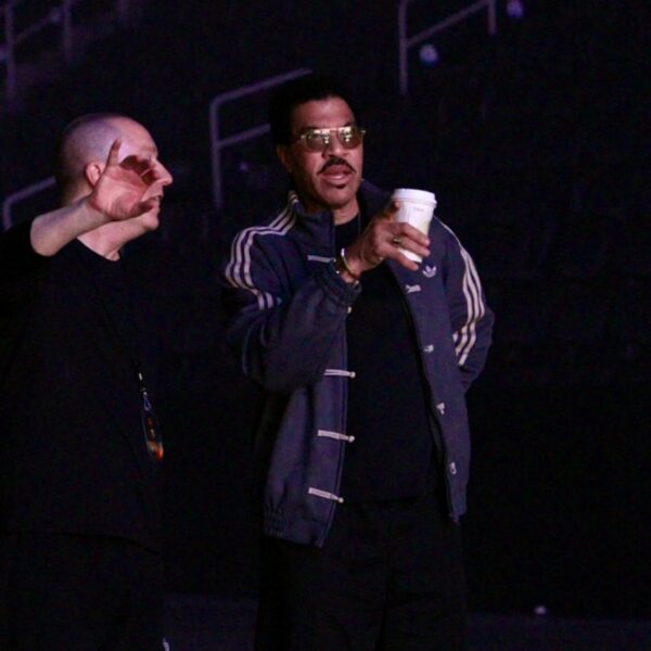 Ο Lionel Richie με ποτήρι στο χέρι, δίπλα σε έναν άνδρα, ετοιμάζεται για την επιστροφή του στη σκηνή.