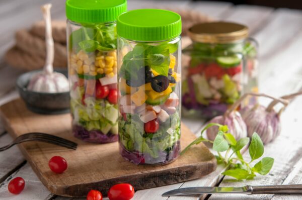 Mason jar salads με layering εμπειρία, γεμάτα φρέσκα υλικά και έτοιμα για κατανάλωση, παρουσιάζονται σε ξύλινη επιφάνεια.