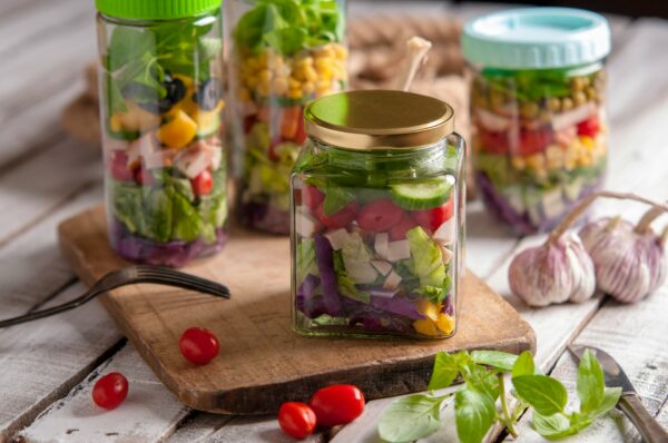 Mason jar salads με στρώσεις λαχανικών και υλικών, έτοιμες για κατανάλωση, παρουσιάζονται σε ξύλο κοπής.