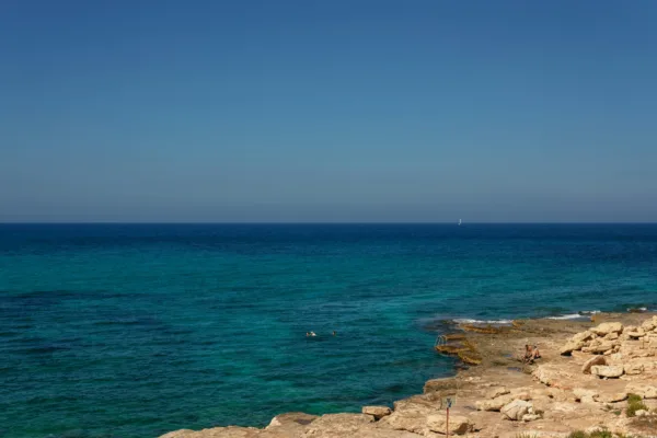 Παραλία στην Αττική με γαλαζοπράσινα νερά και βραχώδη ακτή, ιδανική για βουτιά μετά το γραφείο.