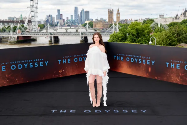 Η Anne Hathaway με λευκό φόρεμα και ψηλές μπότες σε καλοκαιρινή εμφάνιση για την ταινία The Odyssey.