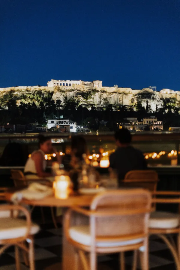 Ζευγάρι απολαμβάνει τη νυχτερινή Αθήνα και την Ακρόπολη από μπαρ της πόλης.