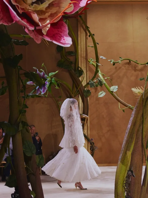 Μοντέλο παρουσιάζει νυφικό σε πασαρέλα Chanel Couture Fall 2026 με σκηνικό από λουλούδια και φυλλώματα.