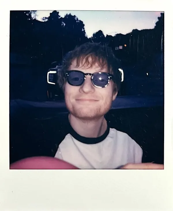 Ο Ed Sheeran με γυαλιά ηλίου χαμογελάει, ενώ ακούει το «Gnarly» των KATSEYE, γράφοντας το επόμενο hit τους.