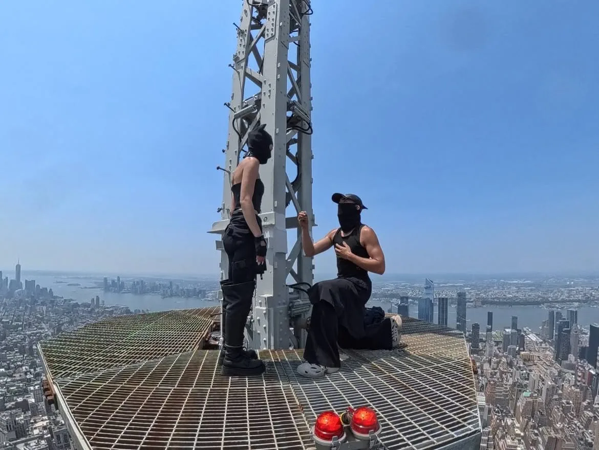 Ζευγάρι κάνει πρόταση γάμου στο Empire State Building σκαρφαλώνοντας σε μεγάλο ύψος, με φόντο την πόλη.