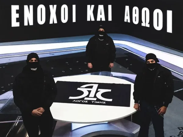 Τρεις καλλιτέχνες του «Λόγος Τιμής» με μαύρα ρούχα και μάσκες στη σκηνή του ΟΑΚΑ.