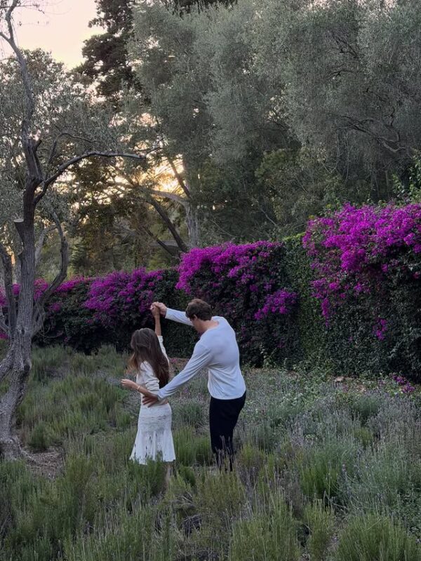 Η Madison Beer και ο αρραβωνιαστικός της Justin Herbert χορεύουν σε έναν κήπο με μπουκαμβίλιες και δέντρα.