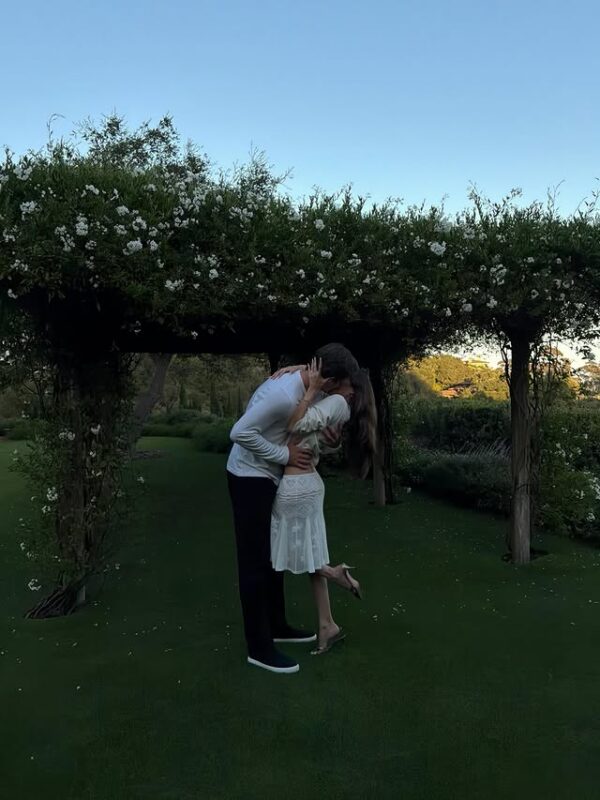Madison Beer και Justin Herbert γιορτάζουν την πρόταση γάμου κάτω από ανθισμένη πέργκολα σε εξωτερικό χώρο.