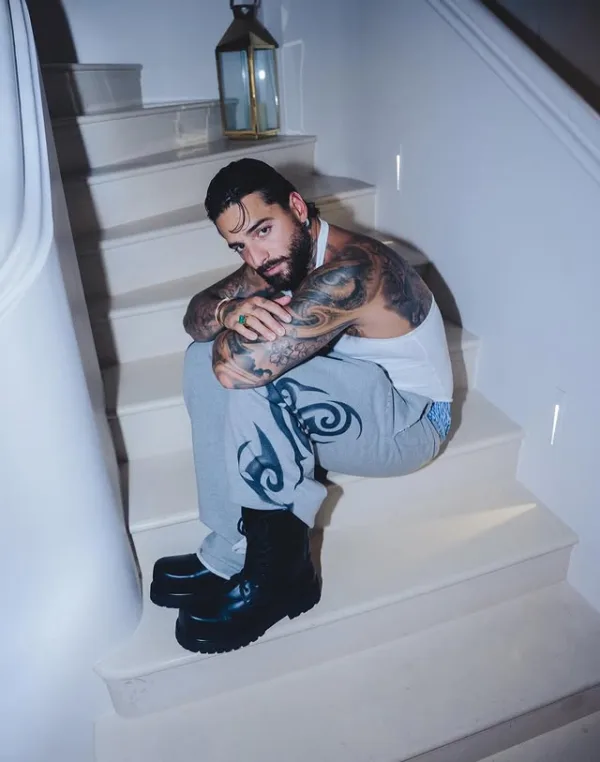 Ο Maluma κάθεται στα σκαλιά φορώντας λευκό φανελάκι και γκρι παντελόνι φόρμας.