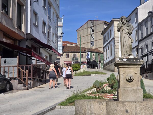 Πεζοπόροι ακολουθούν το Camino de Santiago σε μια πόλη της Ισπανίας, κοντά σε ένα άγαλμα.