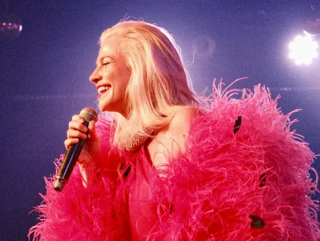 Η Pixie Lott τραγουδάει με μικρόφωνο, φορώντας ένα φόρεμα με φούξια φτερά, κατά την επιστροφή της.
