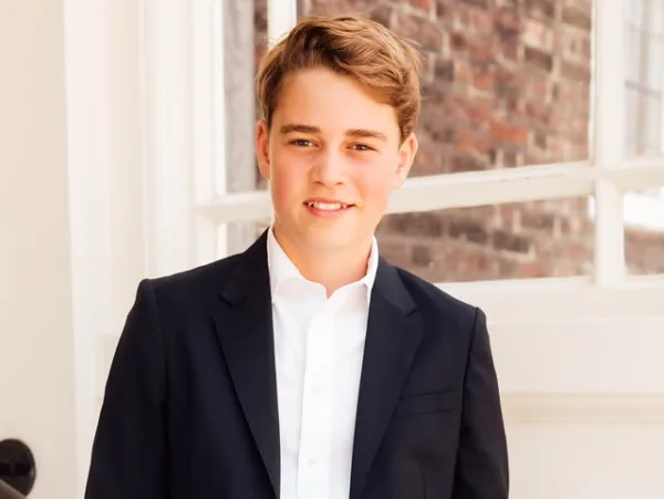 Ο Prince George με κοστούμι και λευκό πουκάμισο χαμογελάει.