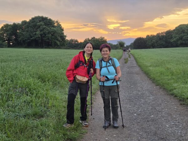 Δύο γυναίκες περπατούν στο Camino de Santiago κατά τη διάρκεια ενός μαγευτικού ηλιοβασιλέματος, απολαμβάνοντας τη φύση.