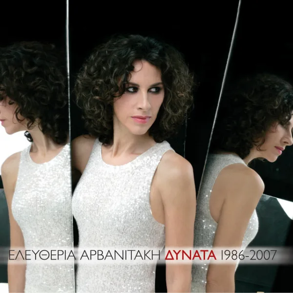 Τραγουδίστρια με σγουρά μαλλιά και λευκό φόρεμα μπροστά από καθρέφτη σε εξώφυλλο δίσκου.