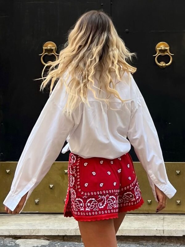 Γυναίκα με λευκό πουκάμισο και σορτς με bandana print, να ποζάρει μπροστά από χρυσή πόρτα.