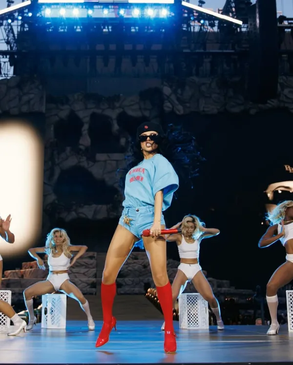 Η Becky G εμφανίζεται στη σκηνή με κόκκινες μπότες και κρατάει μικρόφωνο, προωθώντας το νέο της τραγούδι «Baraja Bendita».