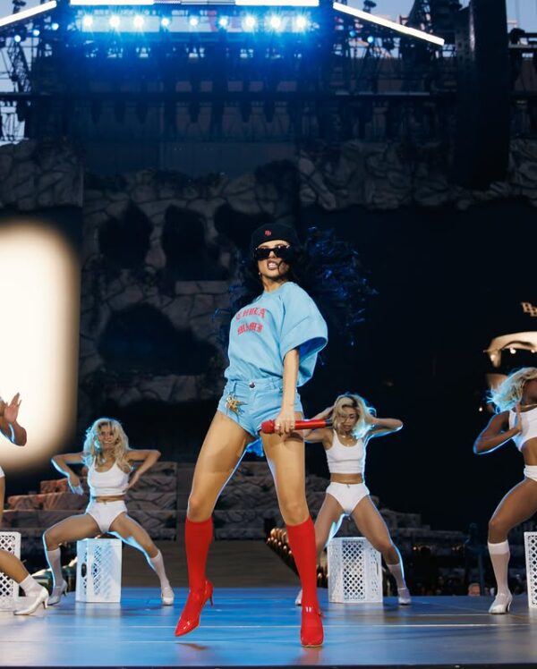 Η Becky G εμφανίζεται στη σκηνή με κόκκινες μπότες και κρατάει μικρόφωνο, προωθώντας το νέο της τραγούδι «Baraja Bendita».